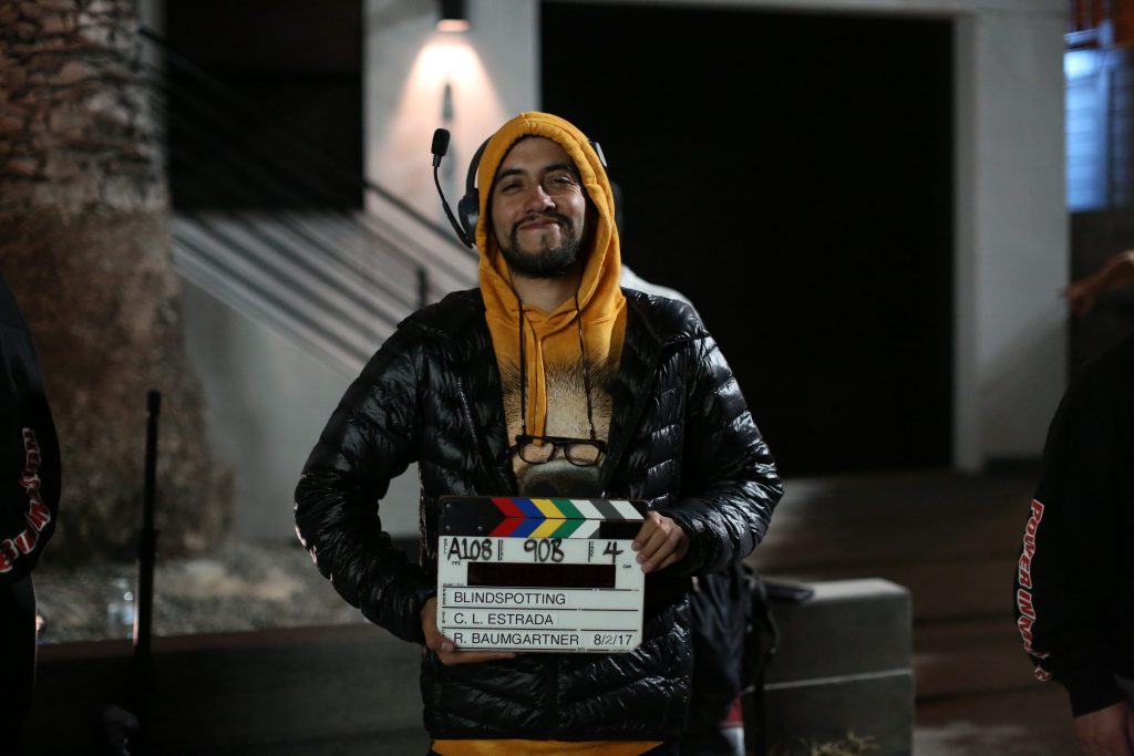 LatinX Man with Leather Jacket and Orange Hat Holding a Director Clapboard