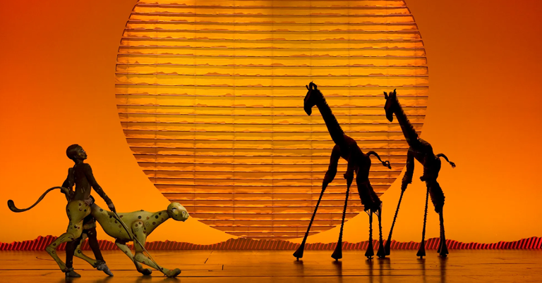 Scene from the Broadway show, The Lion King. Puppeteers moving giraffes and cheetahs on stage.