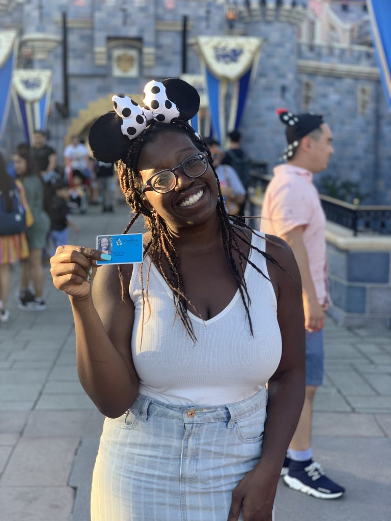 Maureen holding up her employee ID in front of Sleeping Beauty Castle at Disneyland