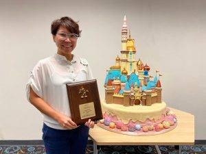 Sam Chan holding an award next to a cake shaped like Honk Kong Disneyland's Castle