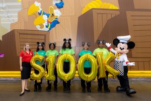Chef Mickey and Disney VoluntEars holding balloons that say $100K