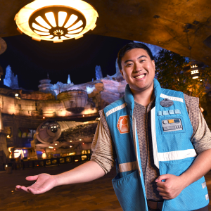 Disney college program operations male cast member smiling and holding out his hand while standing in front of the Millennium Falcon at Smugglers Run at Walt Disney World Resort