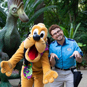 Disney college program entertainment male cast member smiling and standing with his hands imitating animal paws while standing next to Pluto at the Walt Disney World Resort