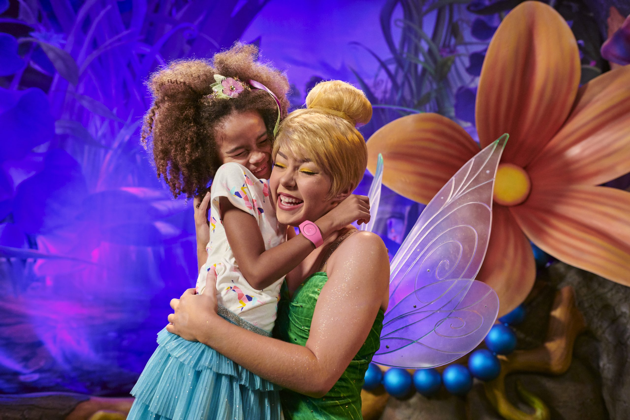 A young Disney Parks guest smiling while hugging a Tinker Bell character performer