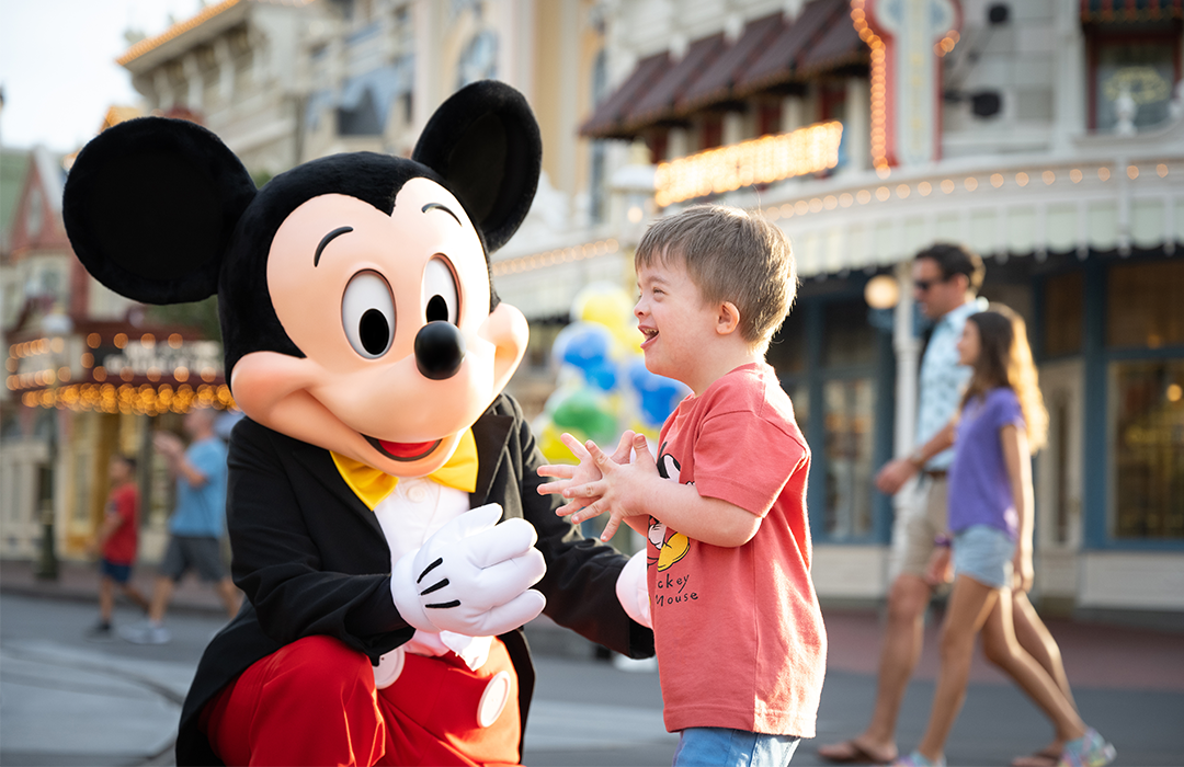 Mickey Mouse character performer kneeling down next to a child guest who is smiling on Main Street at Magic Kingdom