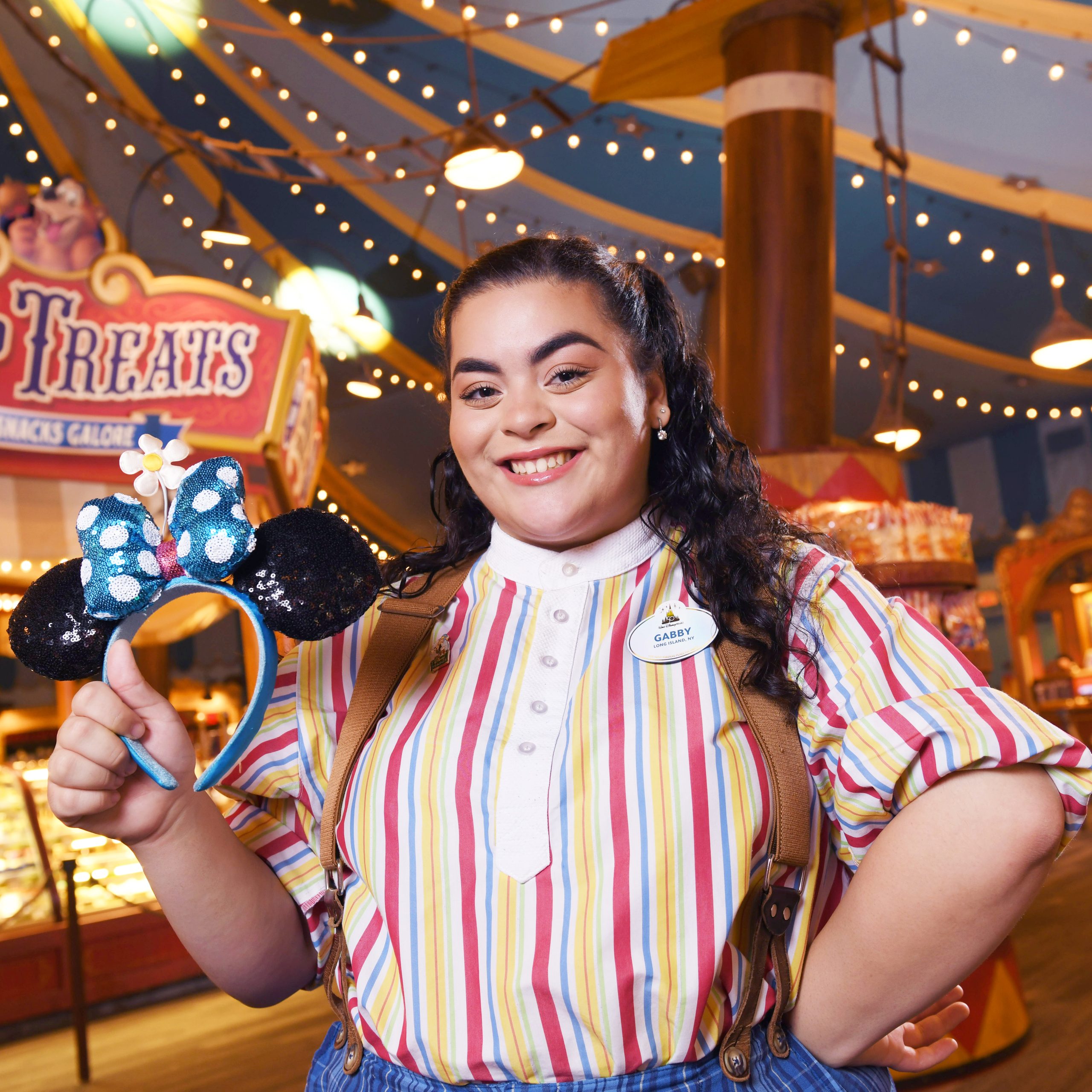 A female Disney College Program participant with long dark hair smiling while holding Minnie Mouse ears in her right hand
