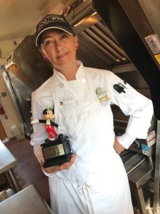 Disney Culinary Sous Chef Cinderella smiling while standing in a kitchen and holding an award statue with Mickey Mouse on it