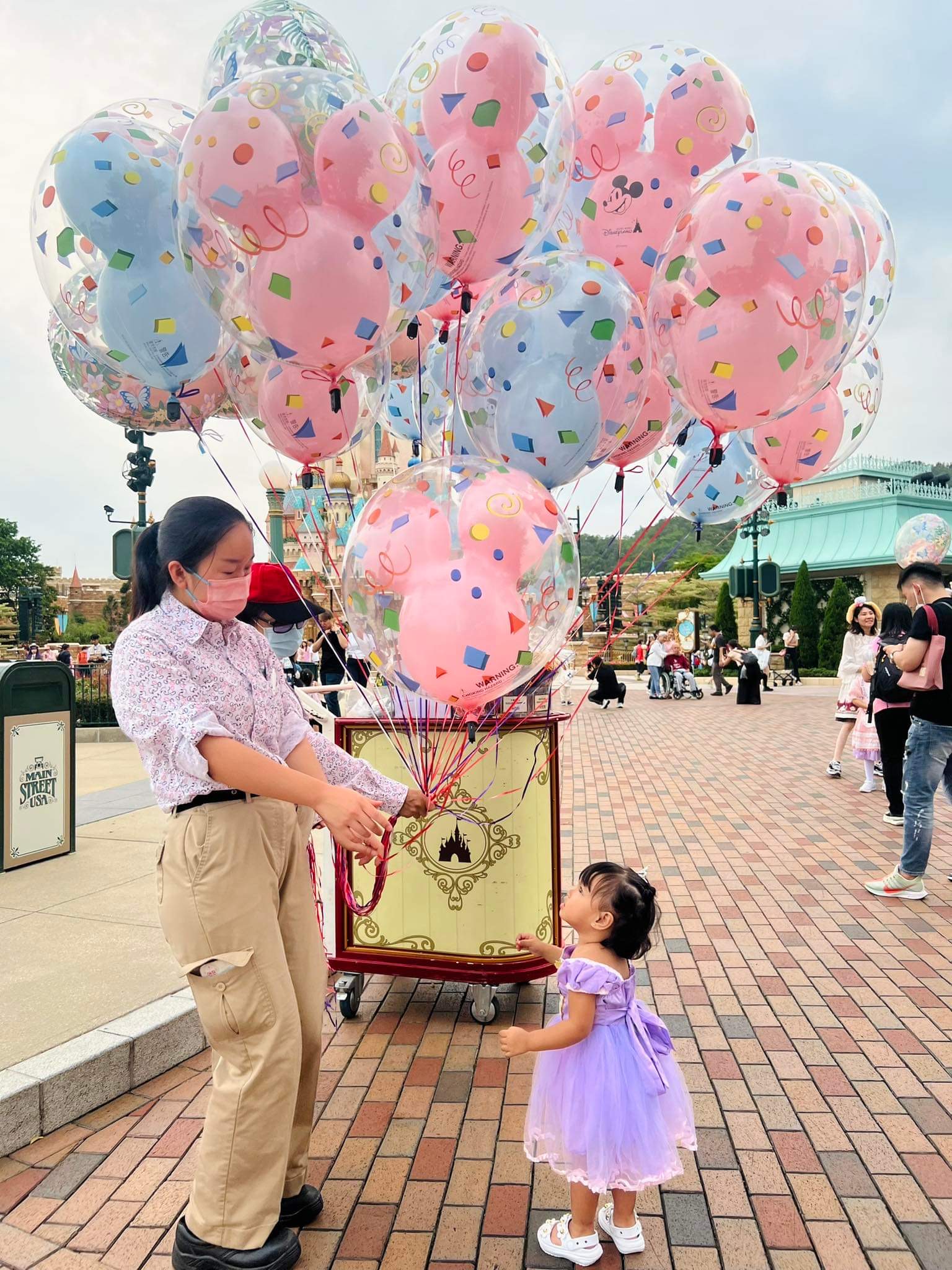 Leovy's small daughter, dressed in a purple princess gown, gets a balloon from a cast member at Hong Kong Disneyland Resort