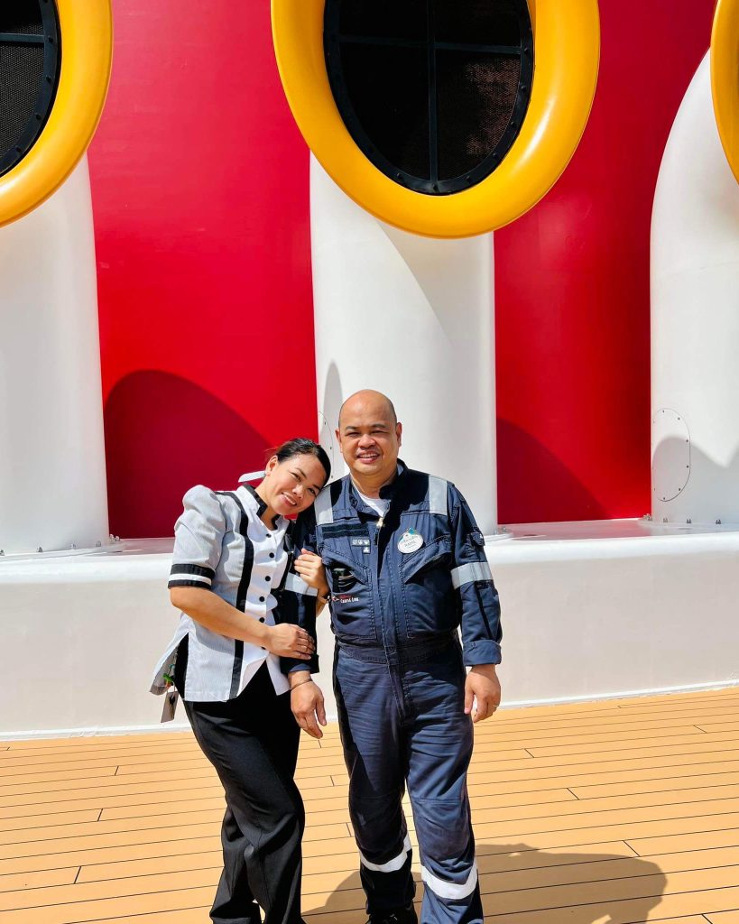 Leovy and Ramil, father and daughter, pose together in their costumes on the Disney Fantasy in front of the iconic red, yellow and white funnel