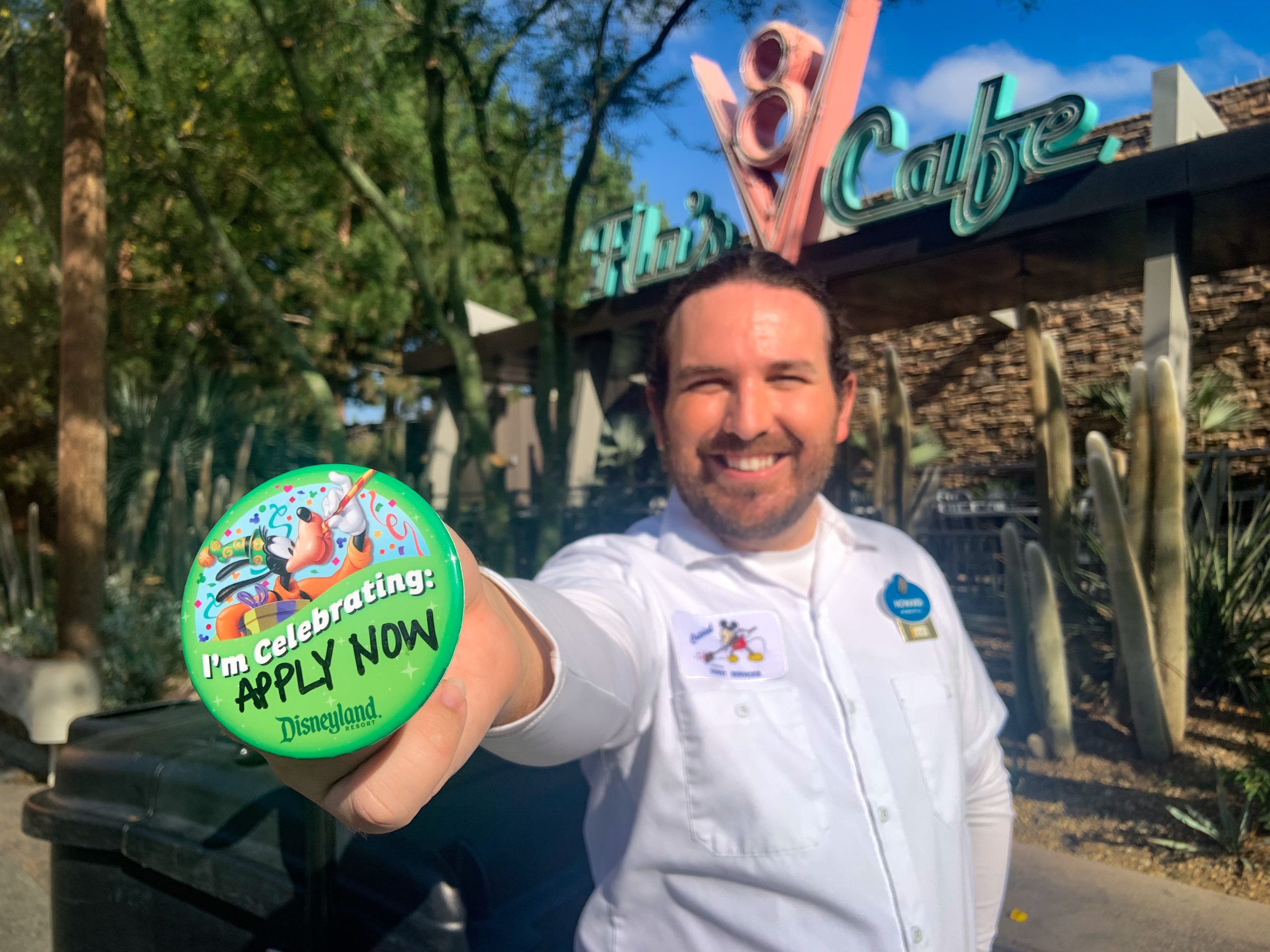 Disneyland Custodial Cast Member Holding Up An I'm Celebrating Button Saying "Apply Now"