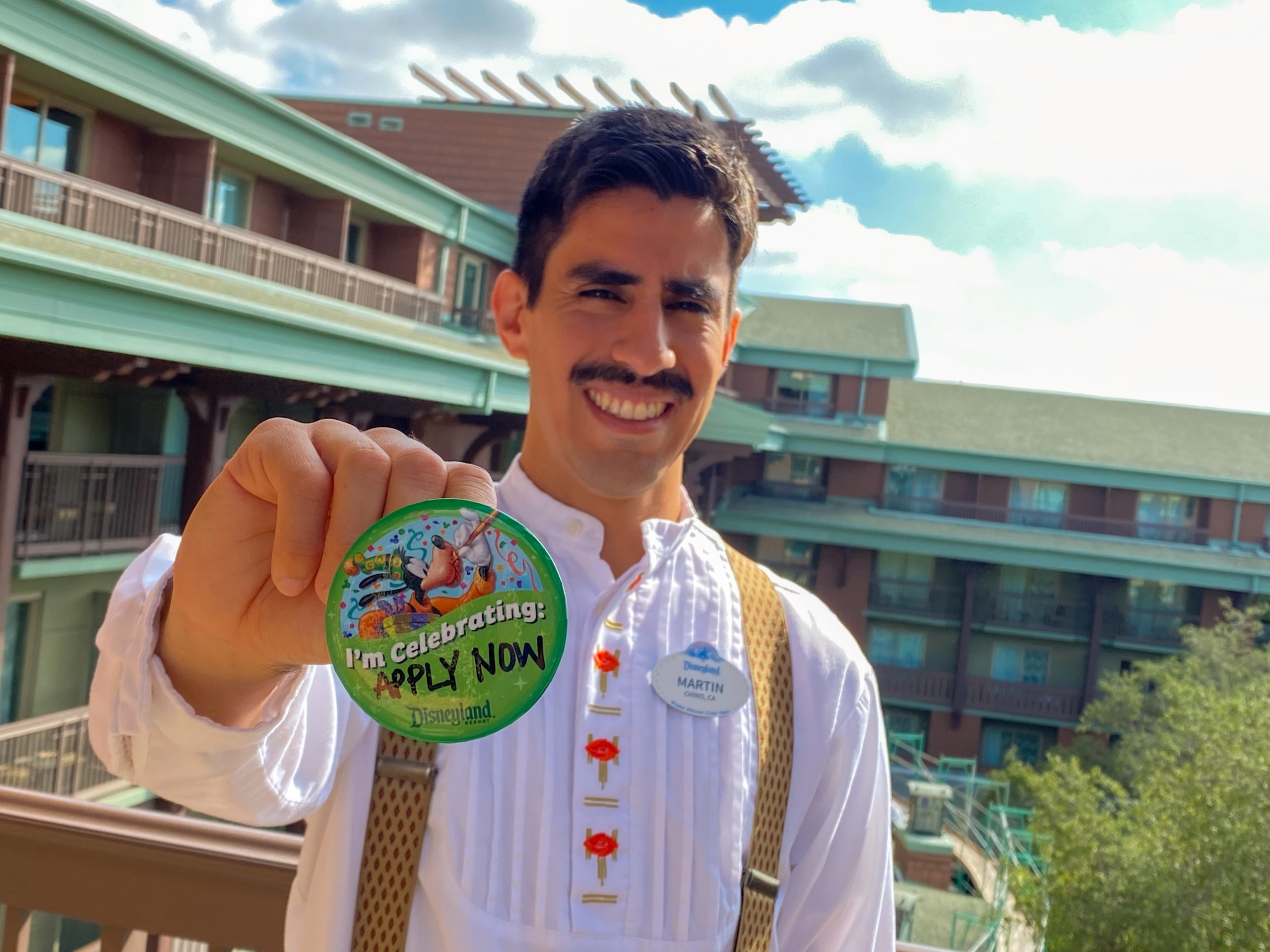 disneyland cast member holding an "im celebrating" button that says "apply now"