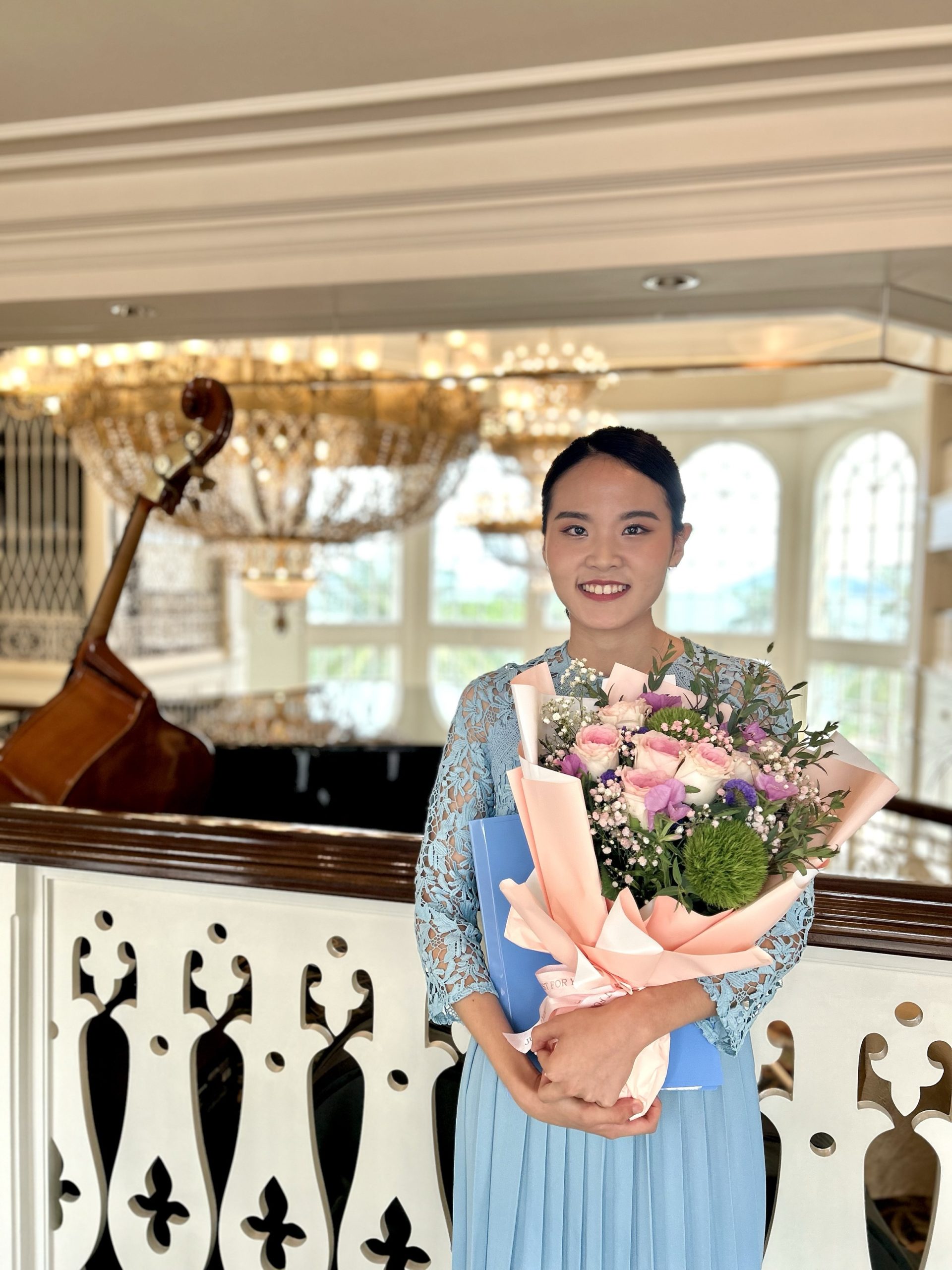 Natalie Yen holding flowers and standing in front of a piano