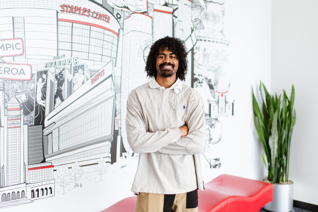 Lenny smiles in front of a mural in the ESPN LA office