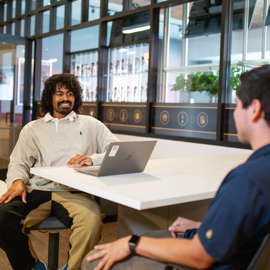 Lenny chats with a colleague while sitting at a table