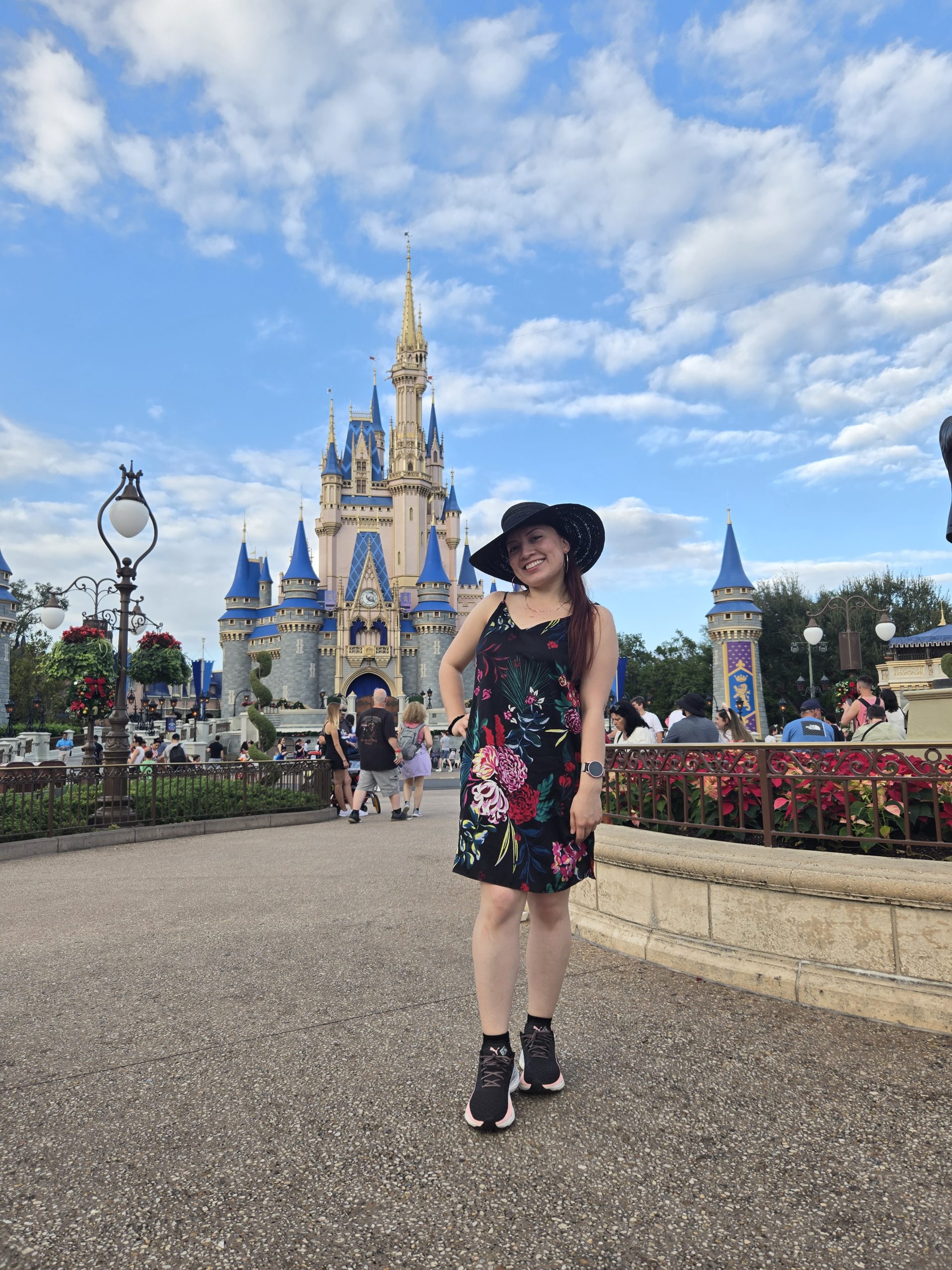 A person in a black hat and floral dress stands in front of Cinderella Castle at Walt Disney World.