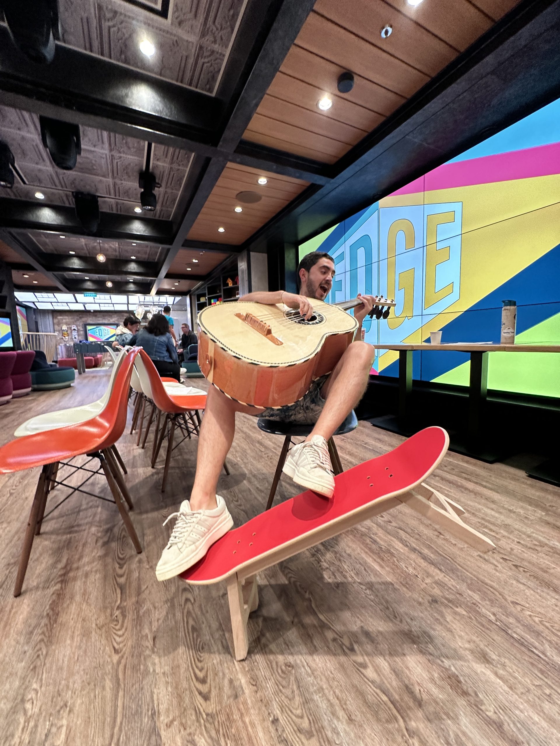 A person sits playing a guitarrón in a colorful indoor space with wooden floors and vibrant wall art.