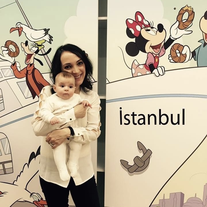 Basak 05 woman holding an infant posing in front of wall with Disney characters