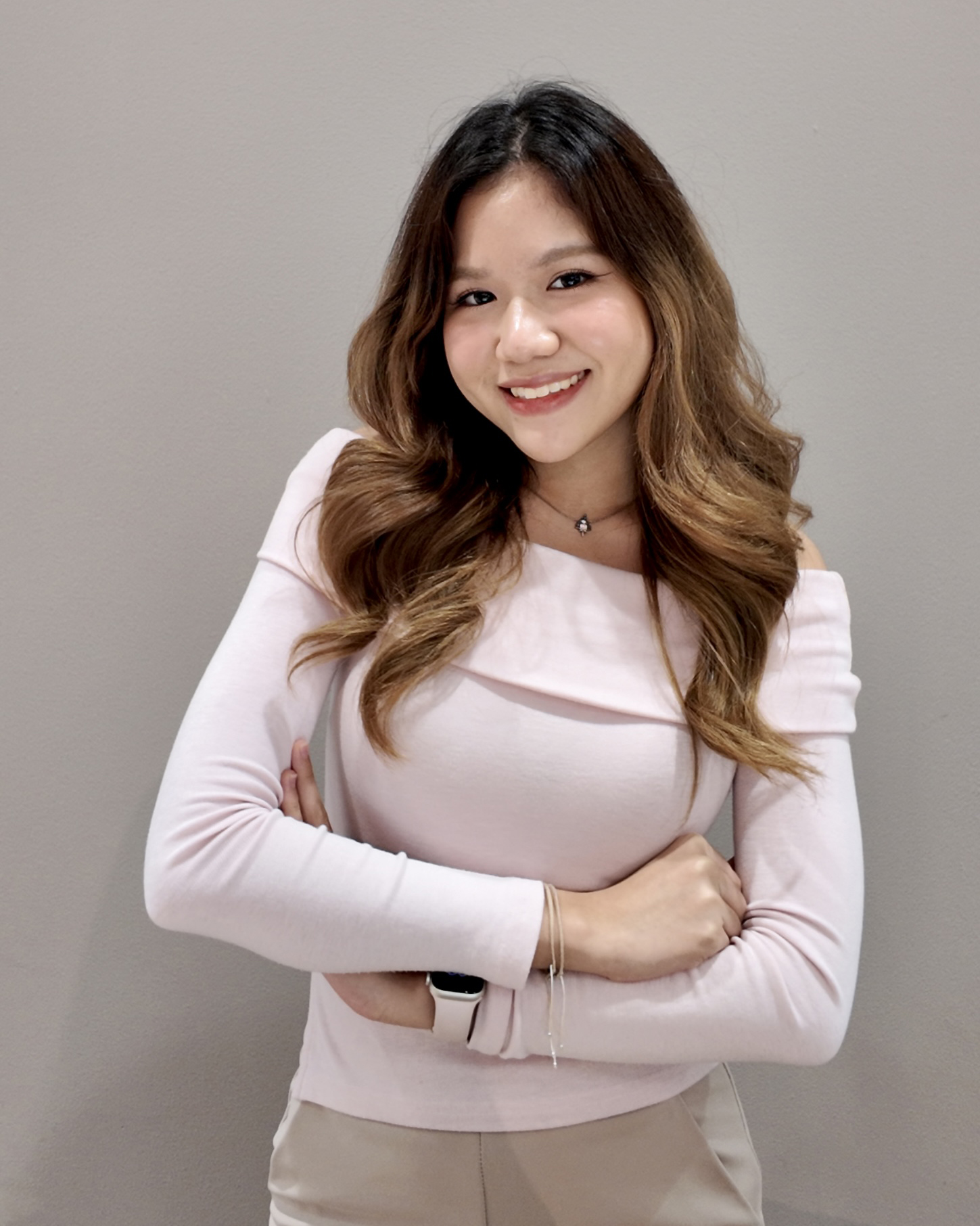 Person with long wavy hair smiling with arms crossed against a plain background.