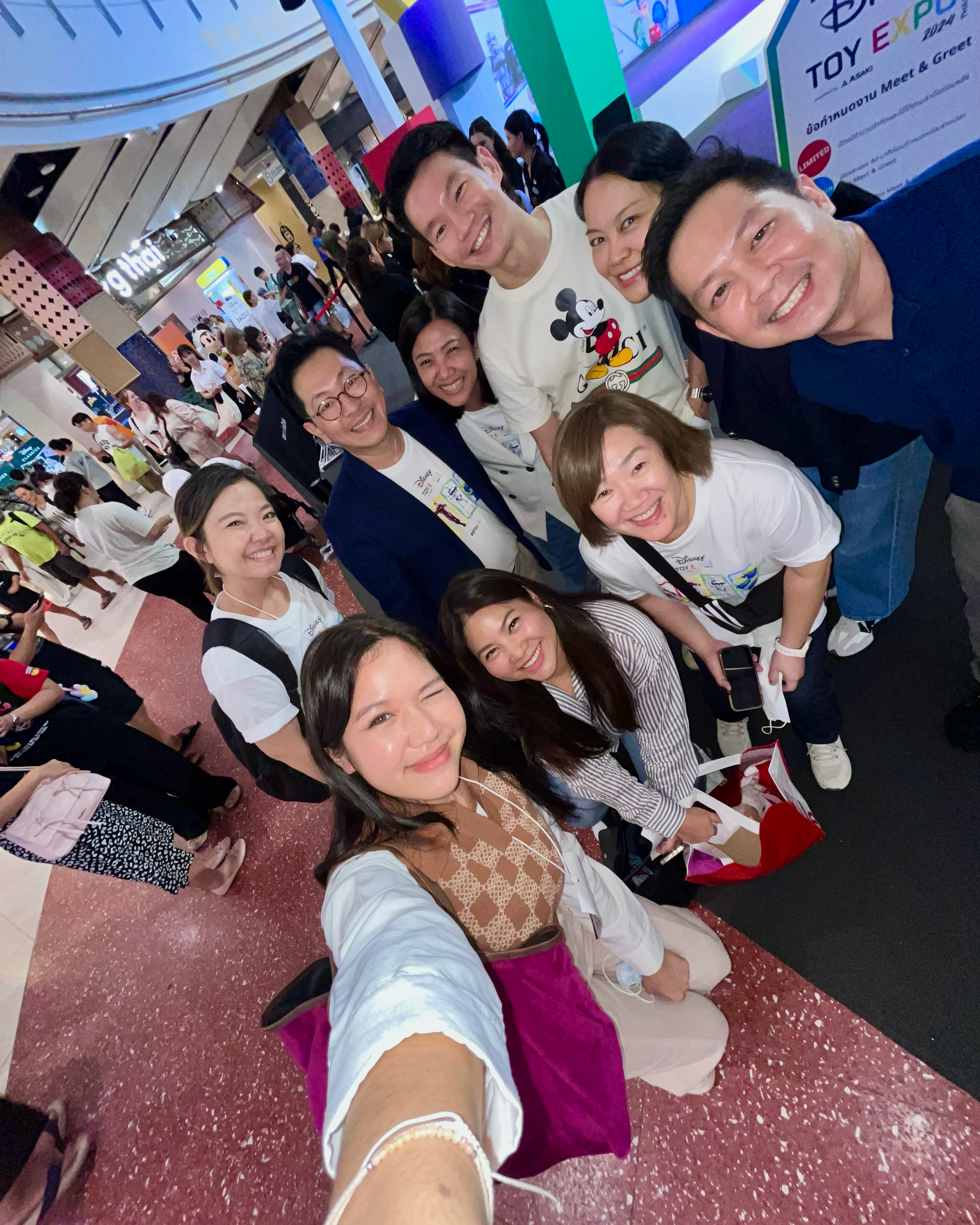 Group selfie at an indoor Toy Expo event, with attendees smiling in front of a sign that reads “TOY EXPO.”