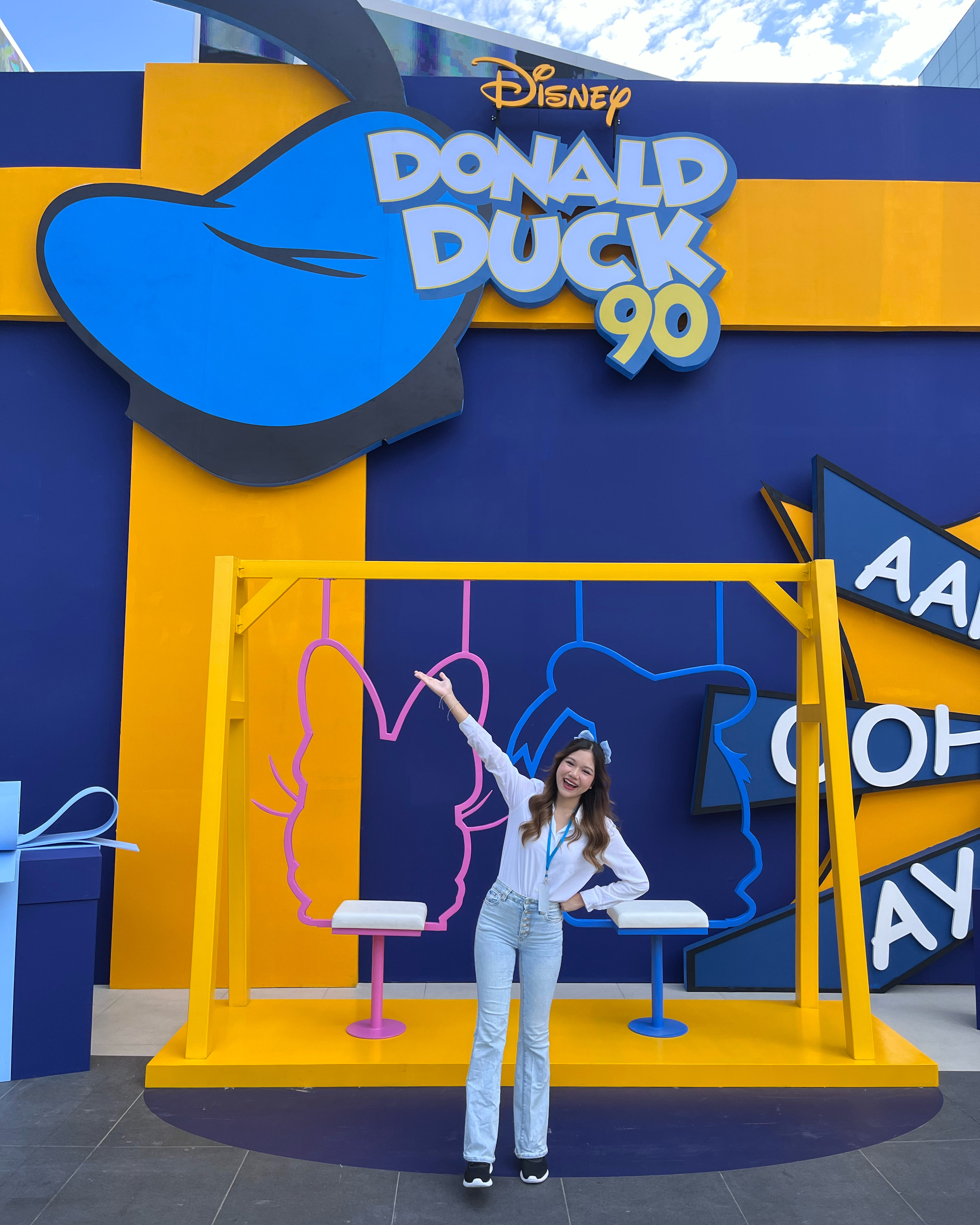 Intern Rosy standing in front of a vibrant display celebrating Donald Duck’s 90th anniversary, featuring Donald’s hat and Disney character outlines on swings.