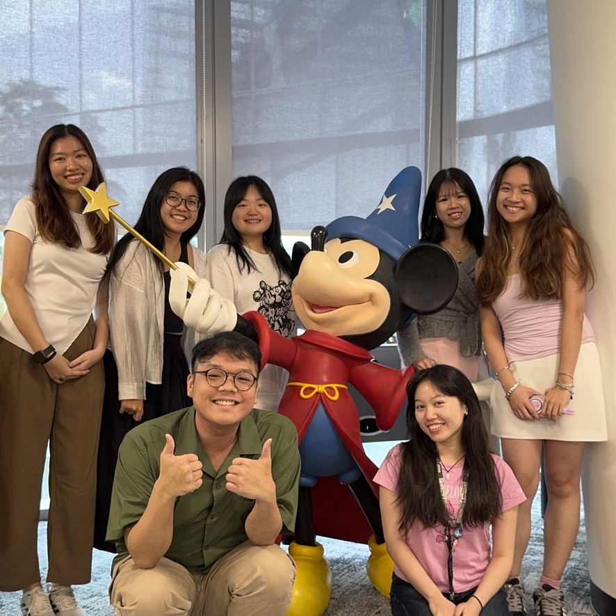 26E1E2DE-7B12-4D62-9BBF-665389601AE9_1_105_c Seven people pose with a large statue of Mickey Mouse dressed as the Sorcerer's Apprentice from Fantasia.