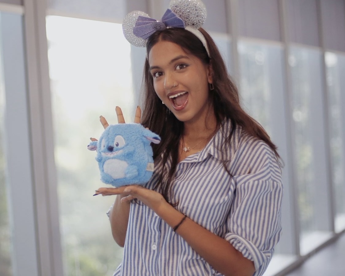 8B361B5C-151A-496A-B8BD-19F882B60461_1_201_a A person wearing Minnie Mouse ears poses excitedly with a Stitch plush toy in a bright office space.