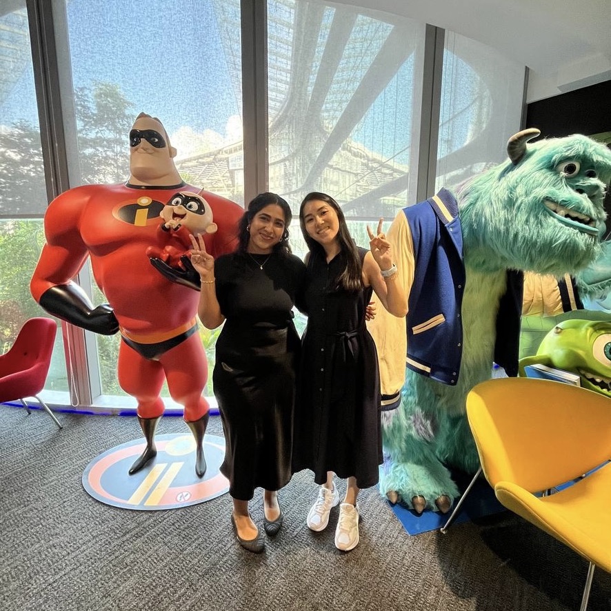 9D6A7806-F2E8-4CA6-9B84-B6509E9207EA_1_105_c Two people pose between statues of Mr. Incredible holding Jack-Jack and Sulley from Monsters Inc. in a bright office space.