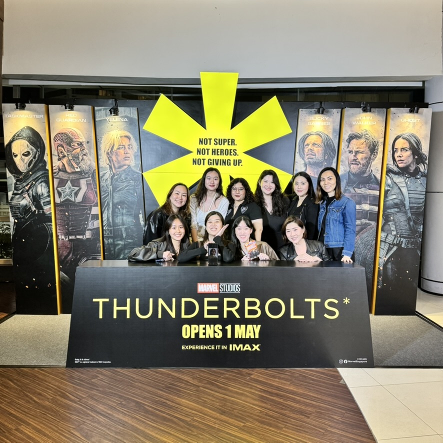 A5561B91-9EE1-49B7-AC90-A1140A75CE19_1_105_c A group poses in front of a "Thunderbolts" movie promo wall featuring character posters and the tagline "Not Super. Not Heroes. Not Giving Up."