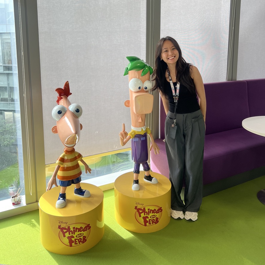 A96496D6-0CA9-497B-8552-1E3D206BC398_1_105_c A person stands beside life-sized statues of Phineas and Ferb in a brightly lit room.