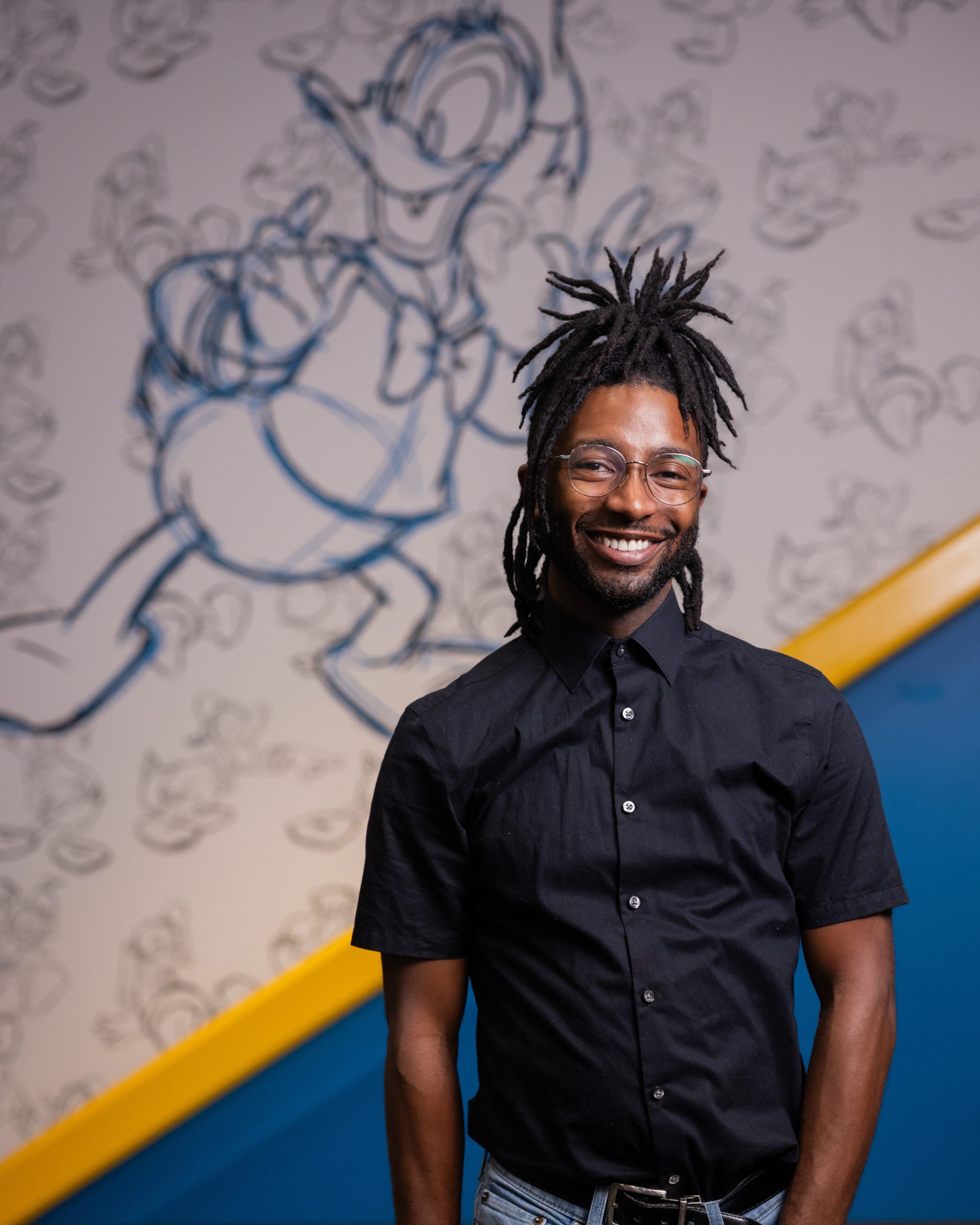 Person standing in front of a wall featuring a large Donald Duck sketch and repeated character illustrations in a themed indoor space.