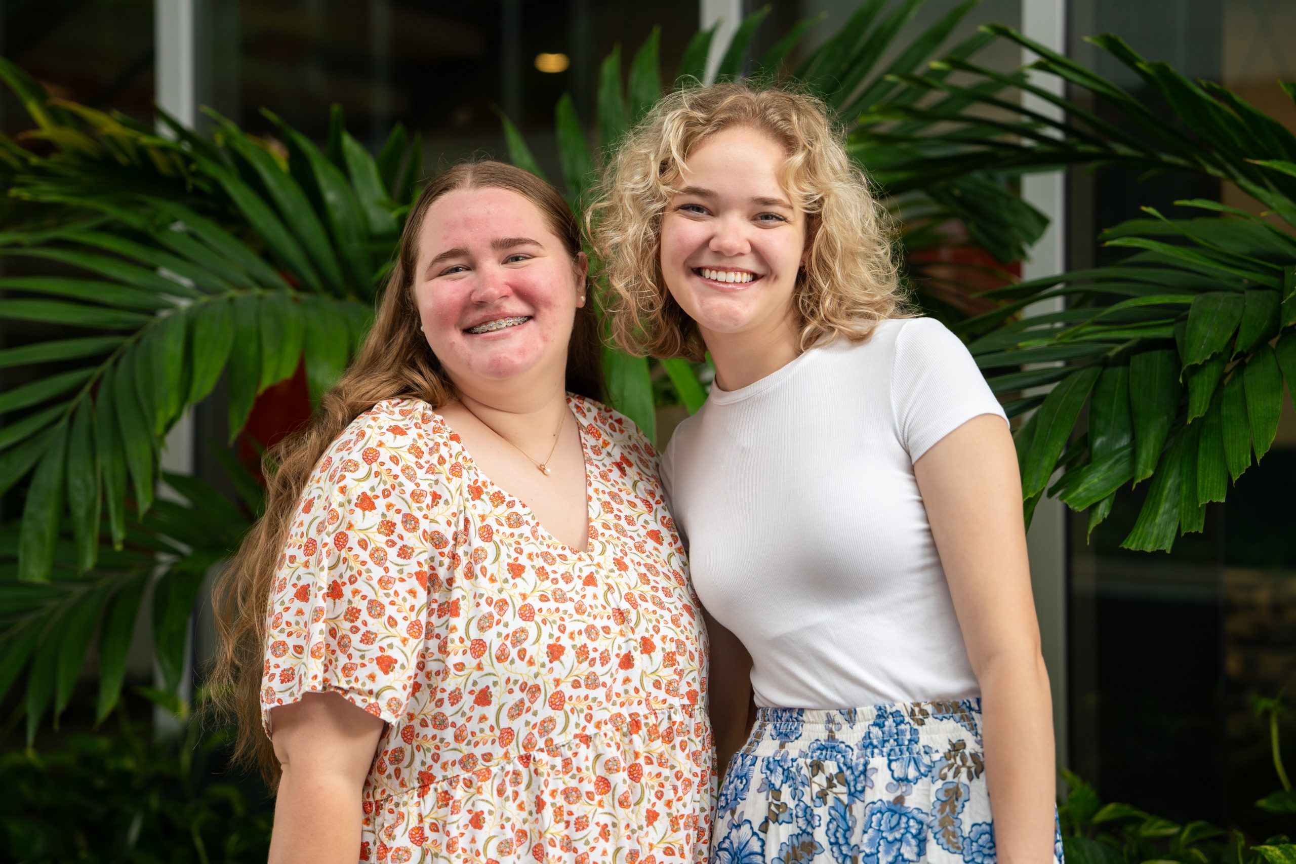 Two people are standing and smiling in front of lush green plants.