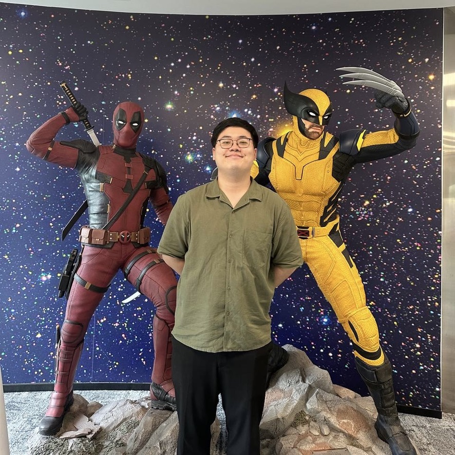 EC4D6C56-79DE-451B-8B10-AA294DEEFCF1_1_105_c A person stands between life-sized statues of Deadpool and Wolverine in an indoor setting with a starry backdrop.