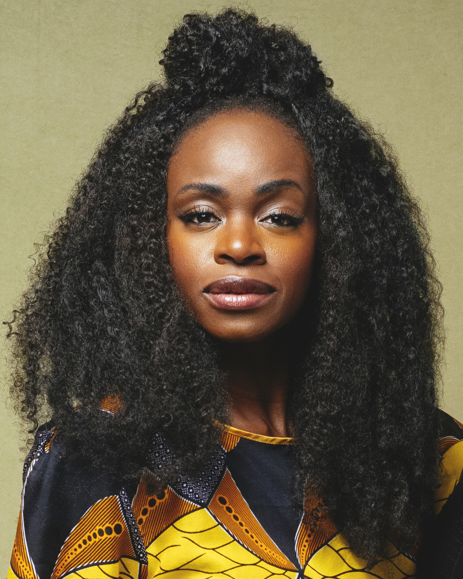 Close-up of a person wearing a vibrant patterned top with textured natural hair against a neutral background.