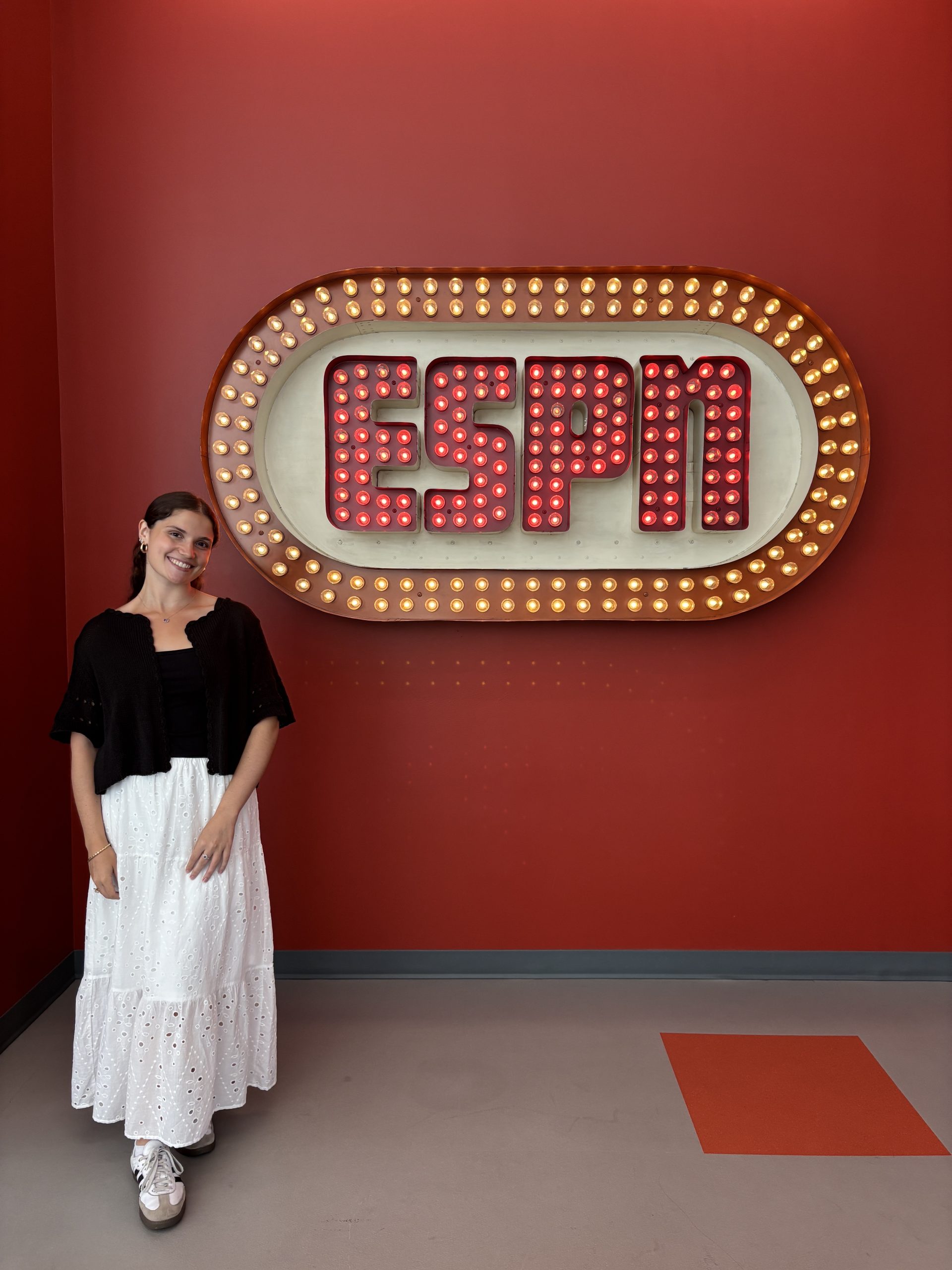 Person standing in front of a retro ESPN sign with illuminated lights on a red wall, representing ESPN’s legacy and vibrant company culture.