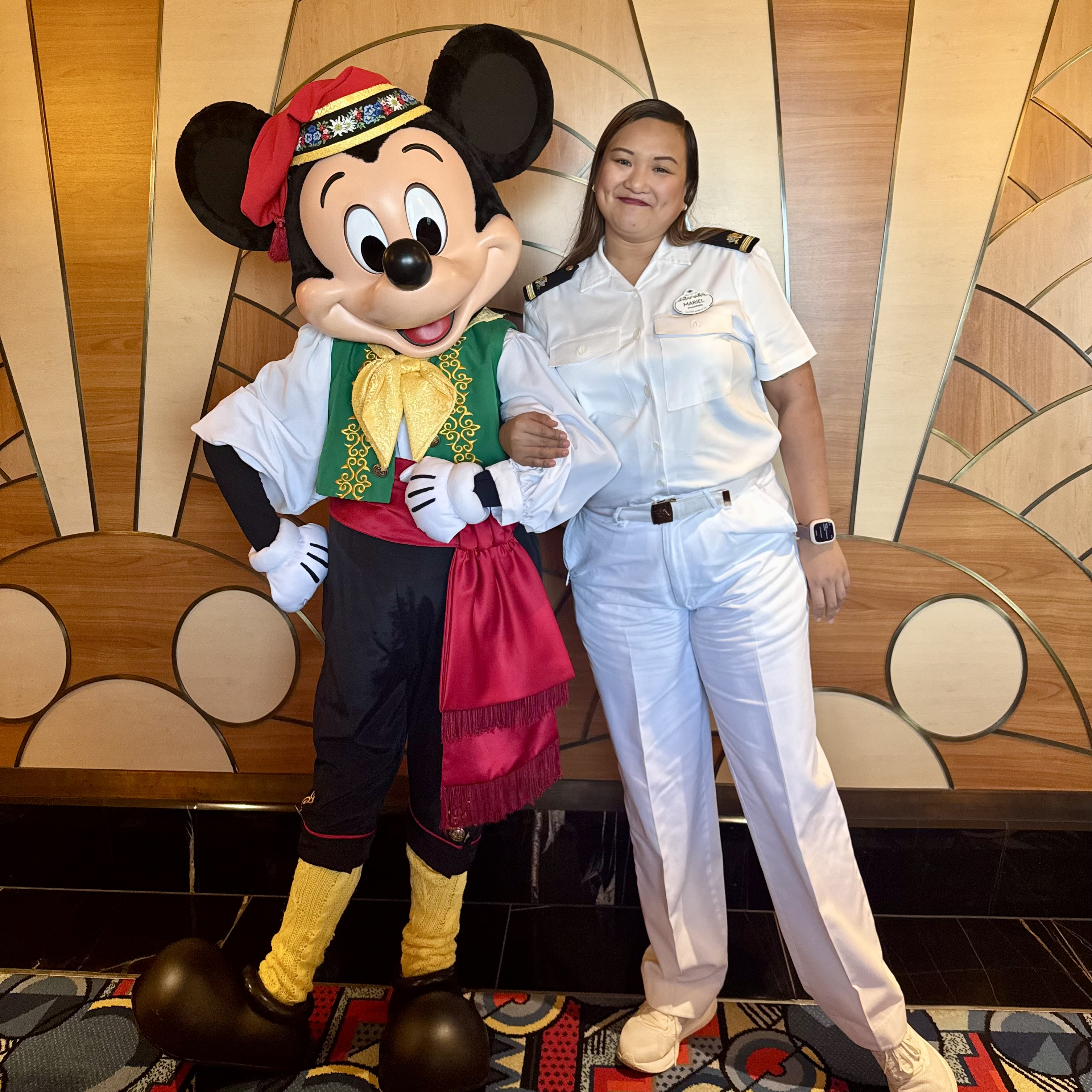 Disney Cruise Line crew member in a crisp white uniform posing with Mickey Mouse in festive pirate attire aboard a Disney cruise ship.