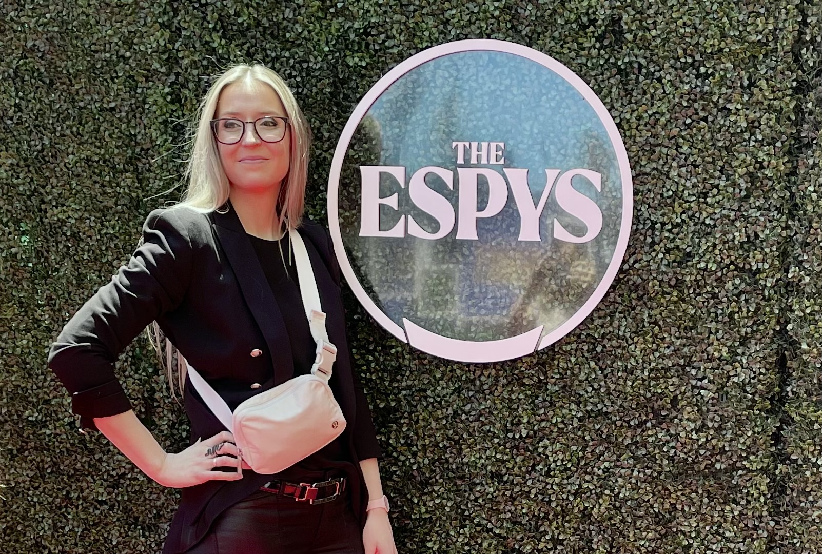 Person standing in front of a circular ESPYS sign on a green wall, showcasing ESPN’s involvement in major sports award events.