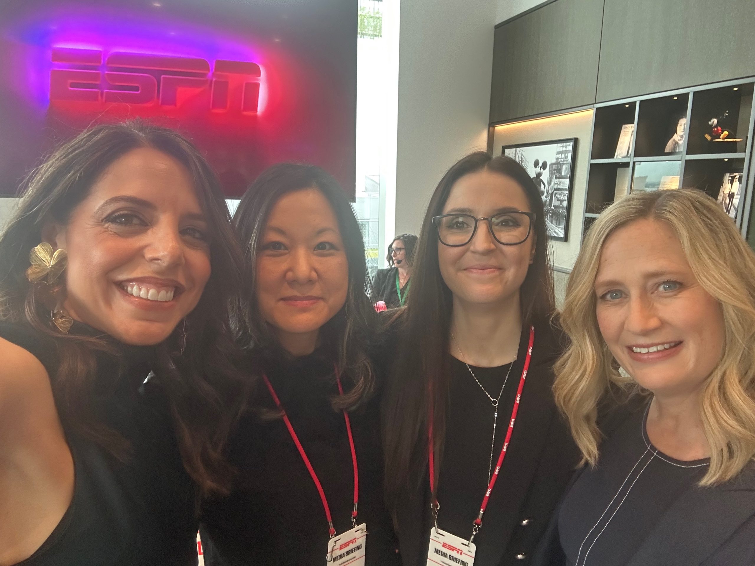 Four people posing in an ESPN office with branded signage and lanyards, reflecting ESPN’s collaborative work culture and team environment.