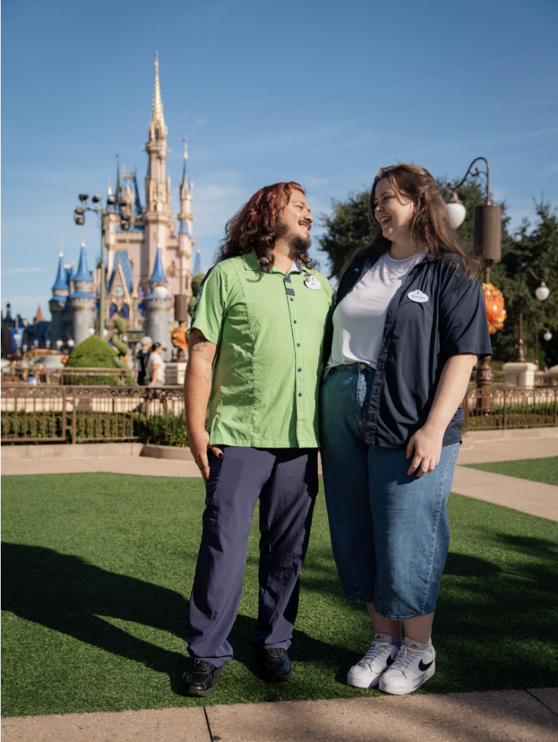 Two people standing together on a pathway with a castle in the background on a sunny day.
