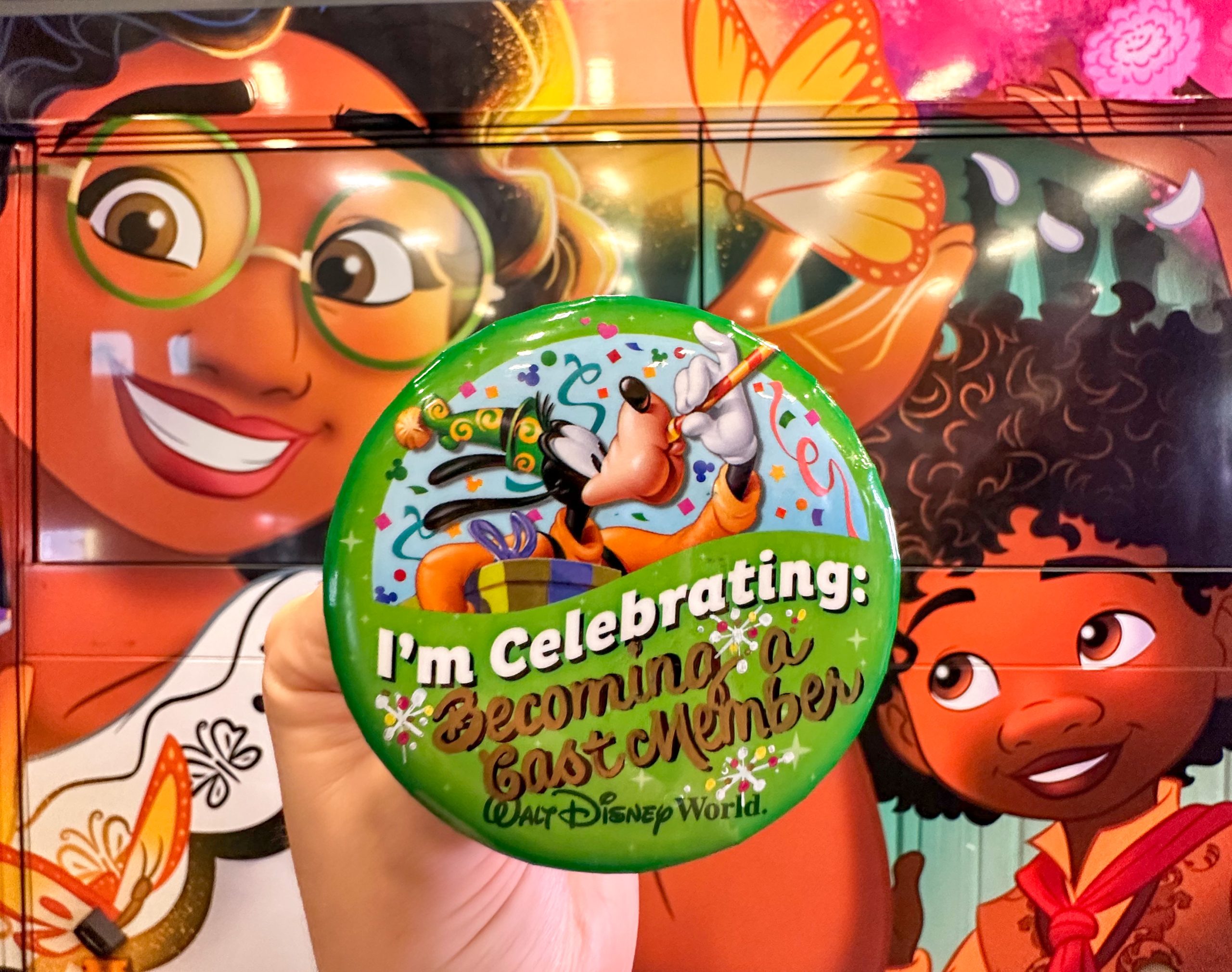 Cast member holding a I'm Celebrating: Becoming a cast member button in front of Disney Bus Transportation
