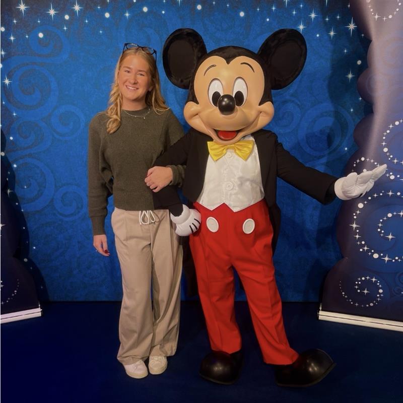 Disney apprentice posing with Mickey Mouse during a character meet-and-greet experience at a Disney location.