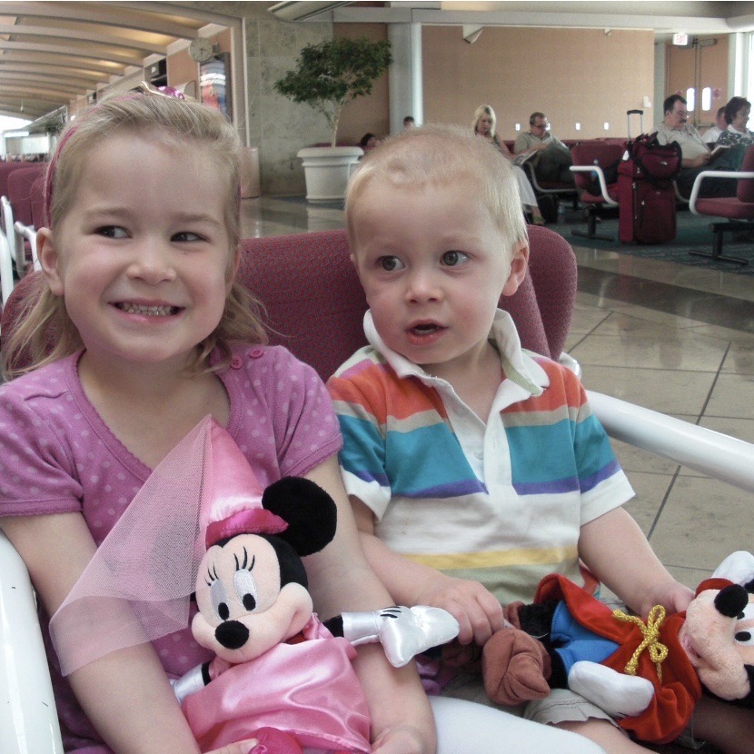 Children seated in an airport holding Minnie Mouse and Mickey Mouse plush toys, reflecting early Disney memories and family travel.