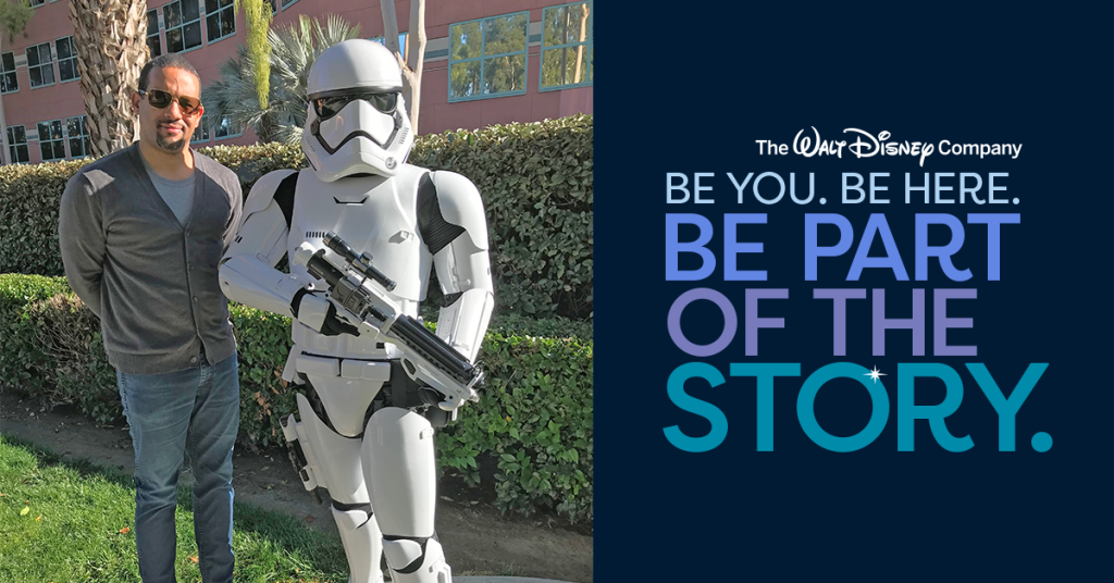Disney employee stands beside a Star Wars Stormtrooper on a landscaped Disney campus next to a &ldquo;Be You. Be Here. Be Part of the Story.&rdquo; Disney Careers brand graphic.