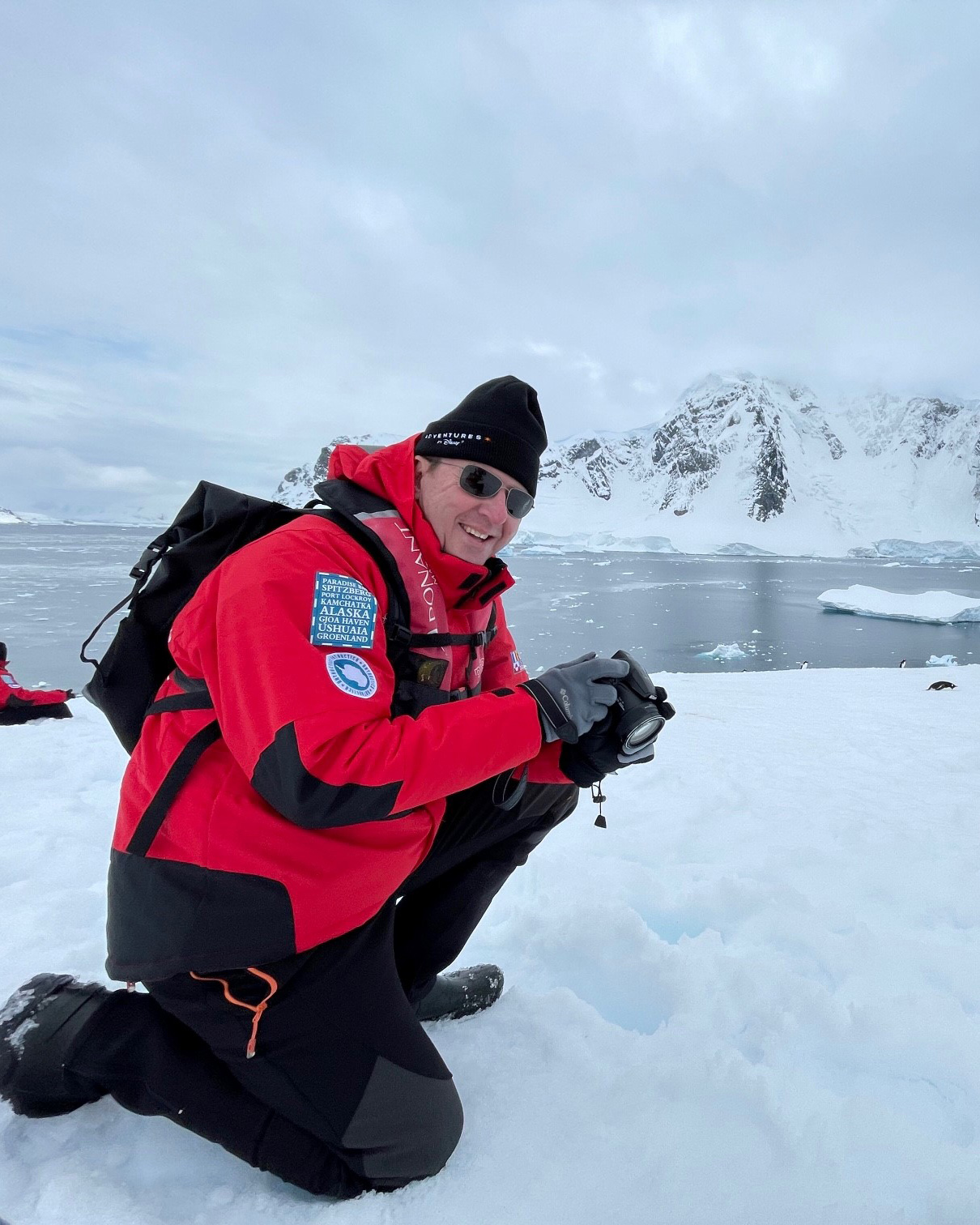 A scientist kneels on Antarctic ice photographing penguins, illustrating real‑world conservation research and science‑led storytelling featured during Earth Month at Disney.