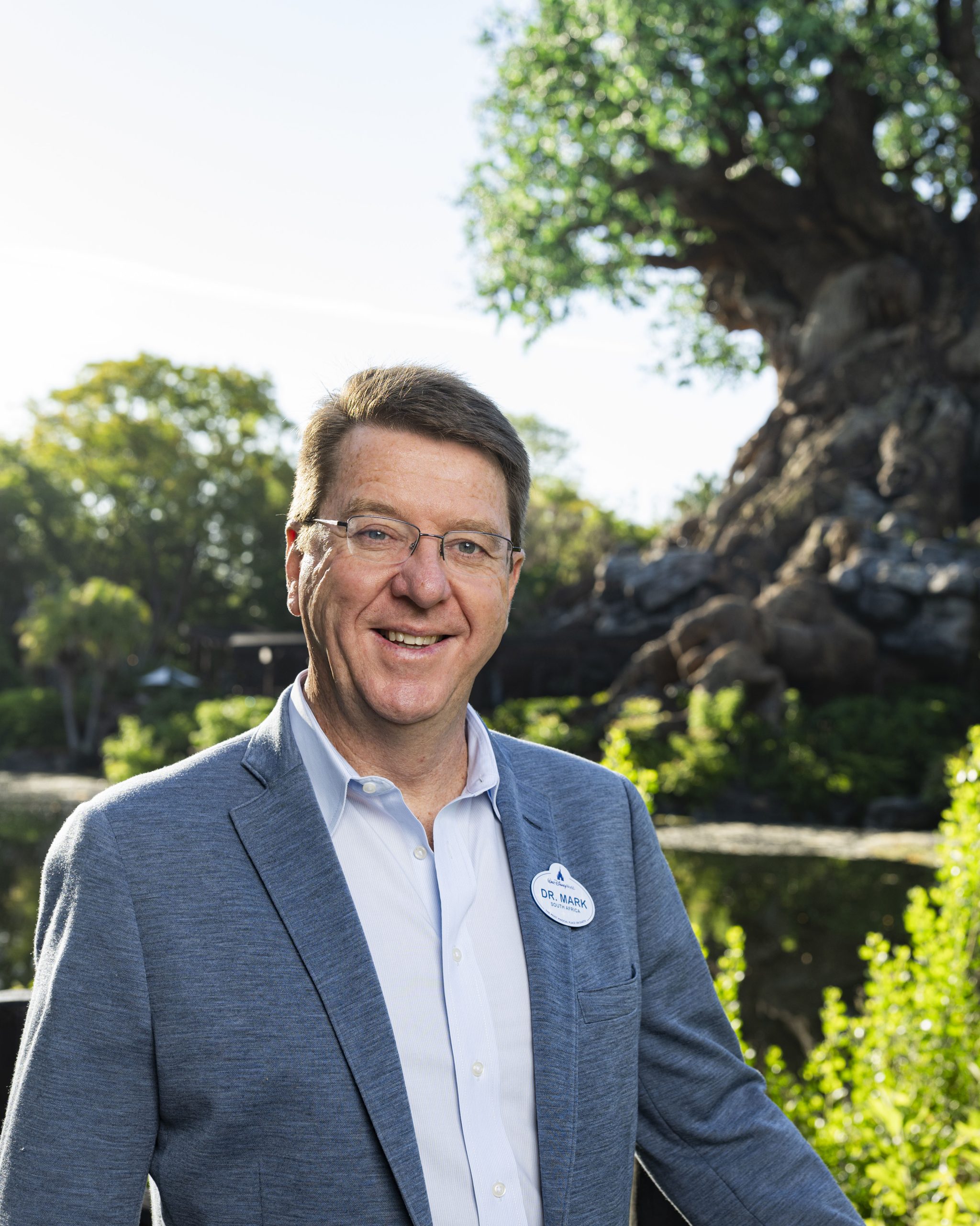 A Life at Disney podcast guest stands outdoors near lush greenery at Disney&rsquo;s Animal Kingdom, reflecting Disney&rsquo;s commitment to conservation and animal science.