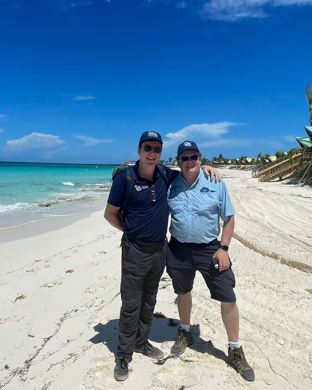 Two conservation team members stand on a beach near turquoise water during a field expedition, reflecting global wildlife research and conservation efforts supported by Disney.