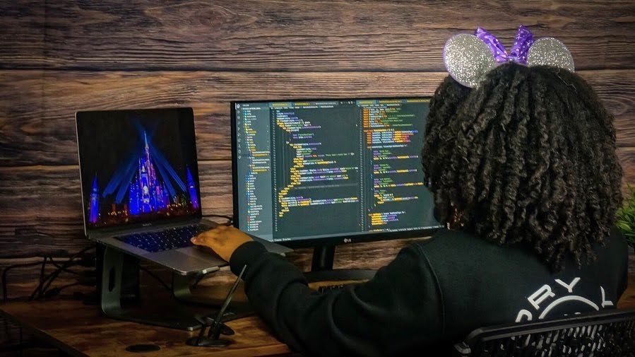 April, seen from behind, works on code on her computer.