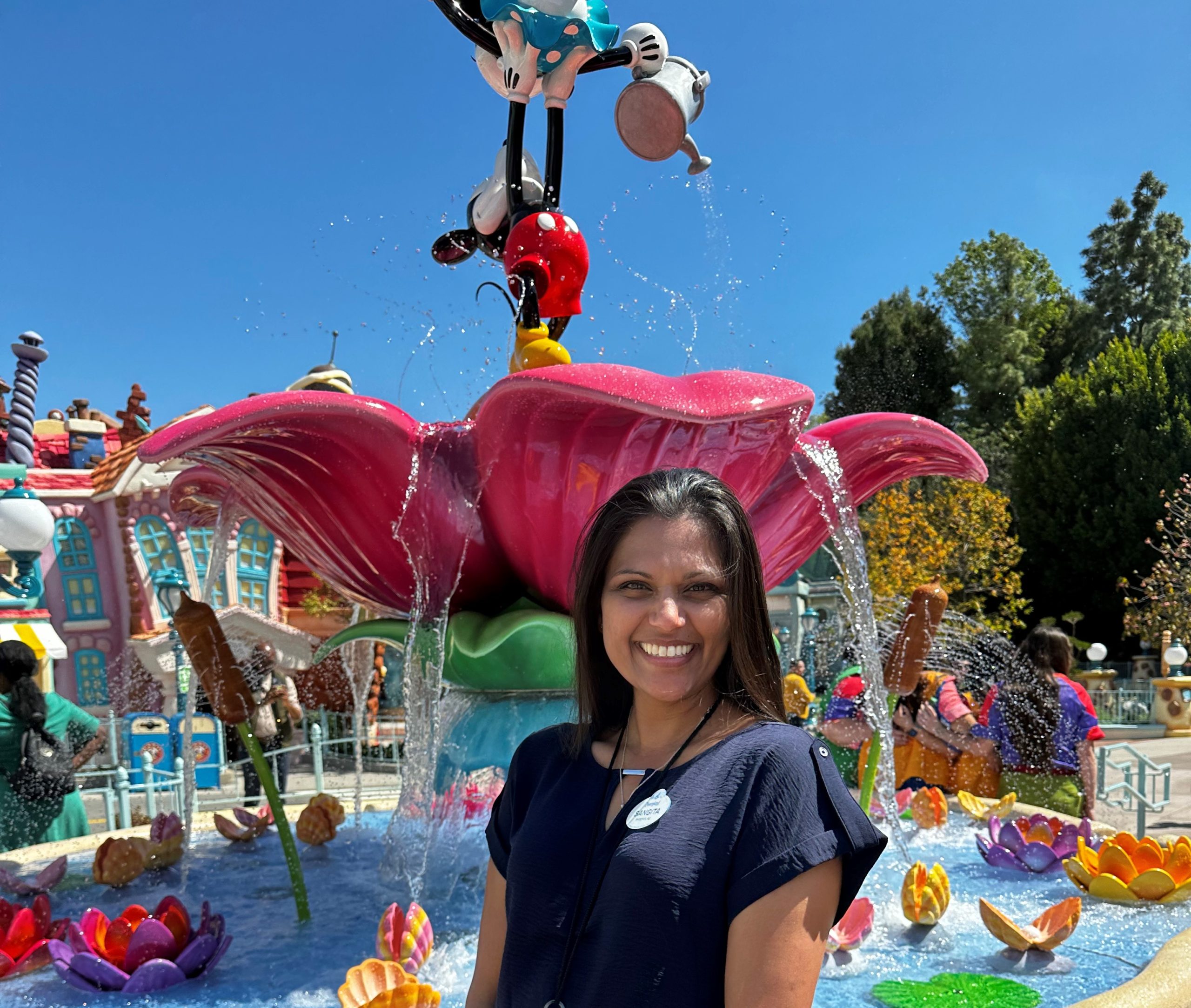 Sangita smiling in front of Mickey and Minnie water fountain in ToonTown.