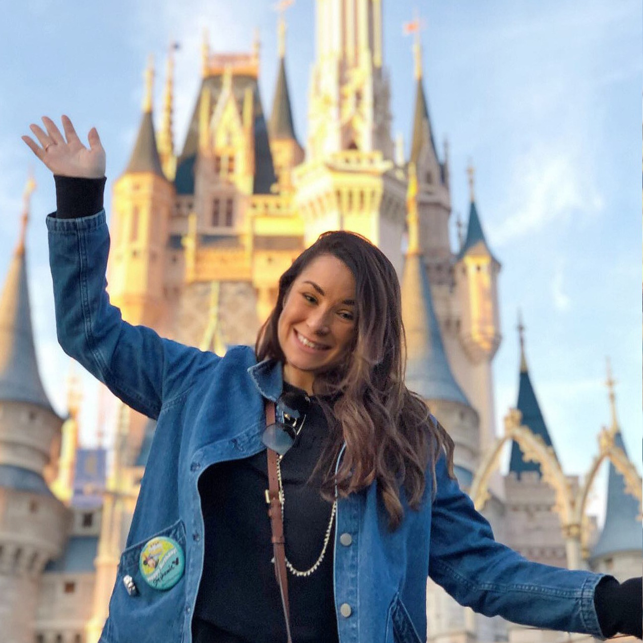 A Disney employee smiles and waves in front of Cinderella Castle at Walt Disney World, celebrating career journeys, employee pride, and working at The Walt Disney Company.