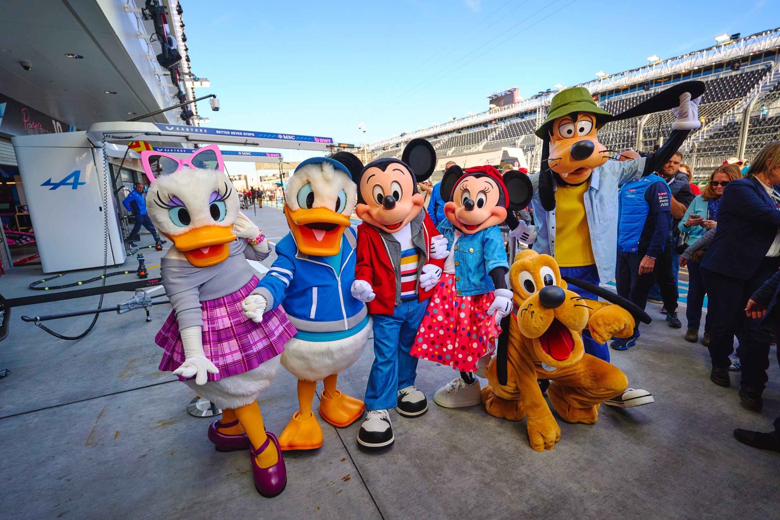 Mickey Mouse, Donald Duck, Daisy Duck, Goofy, and Pluto appear at a Formula 1 race activation showcasing the Disney Consumer Products collaboration.