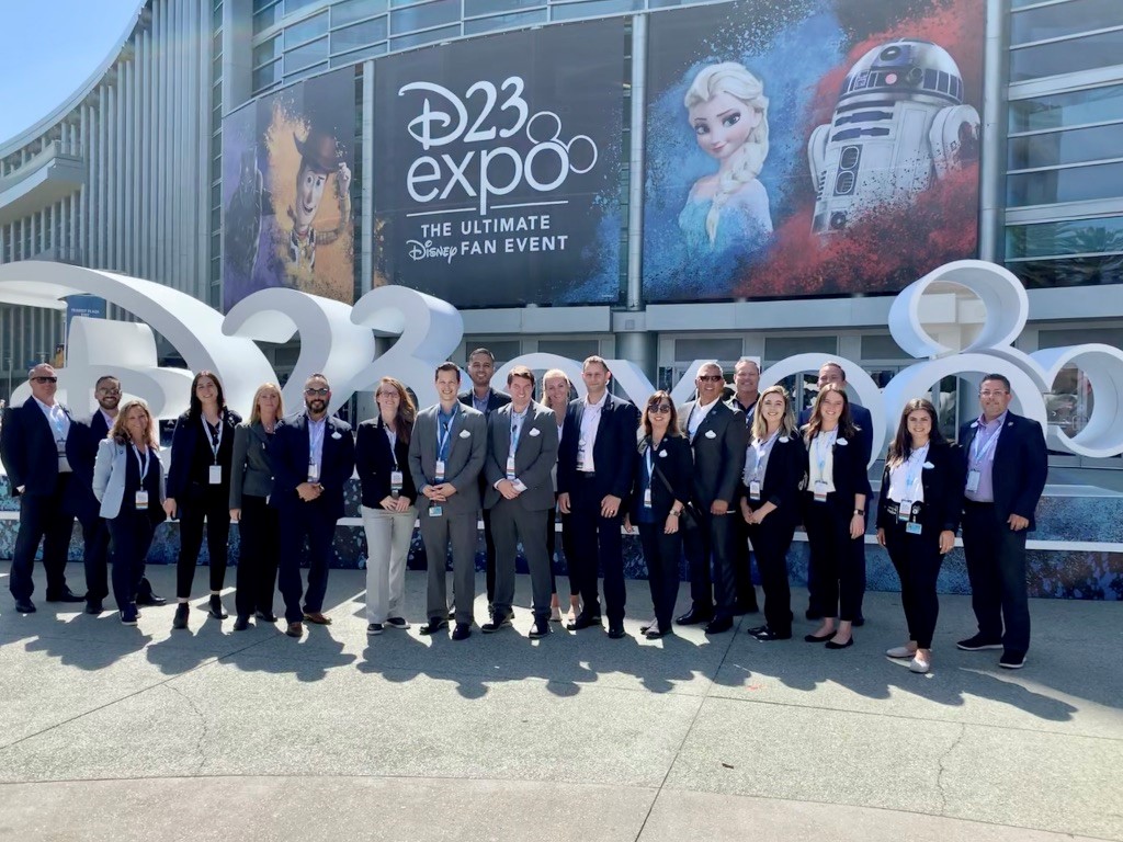 A group of Disney employees stand in front of D23 Expo signage.